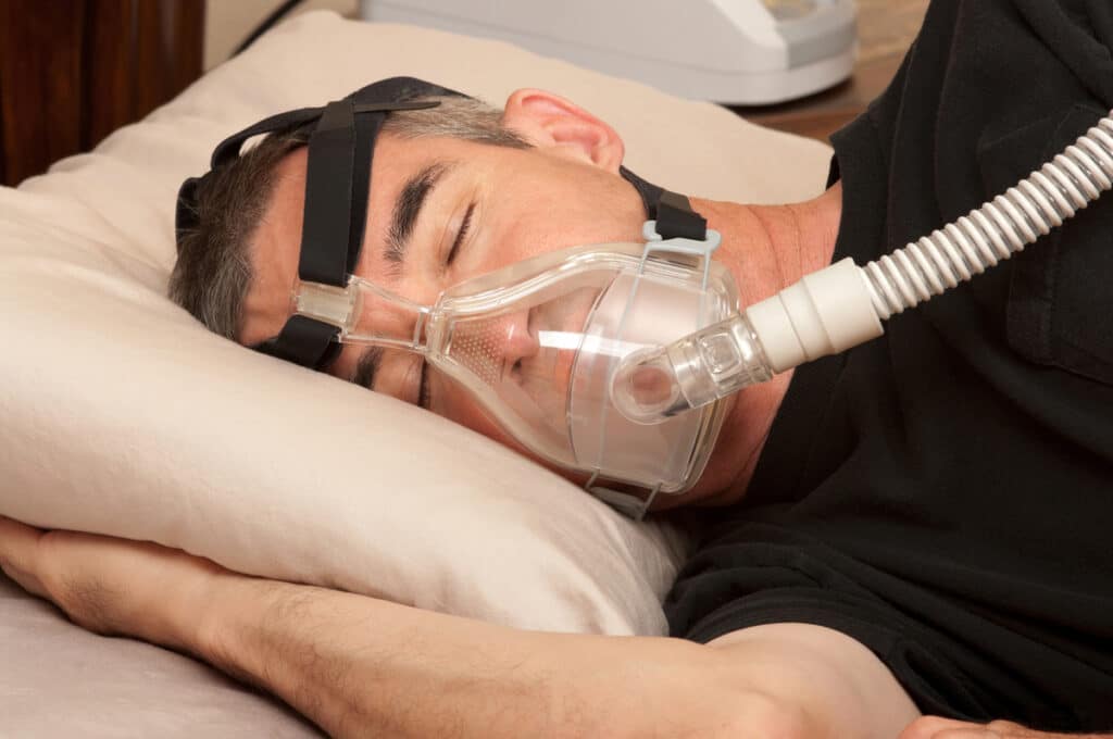 A Man Sleeping With A Cpap Mask As Part Of An Effective Treatment For Sleep Apnea, Ensuring Proper Airflow And Improved Sleep Quality.