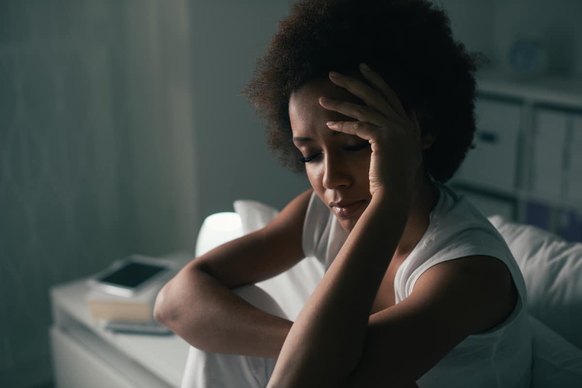 A Woman Sitting On Her Bed At Night, Visibly Distressed, Symbolizing The Challenges Of Sleep Disorders Such As Insomnia And Their Impact On Sleep Quality.