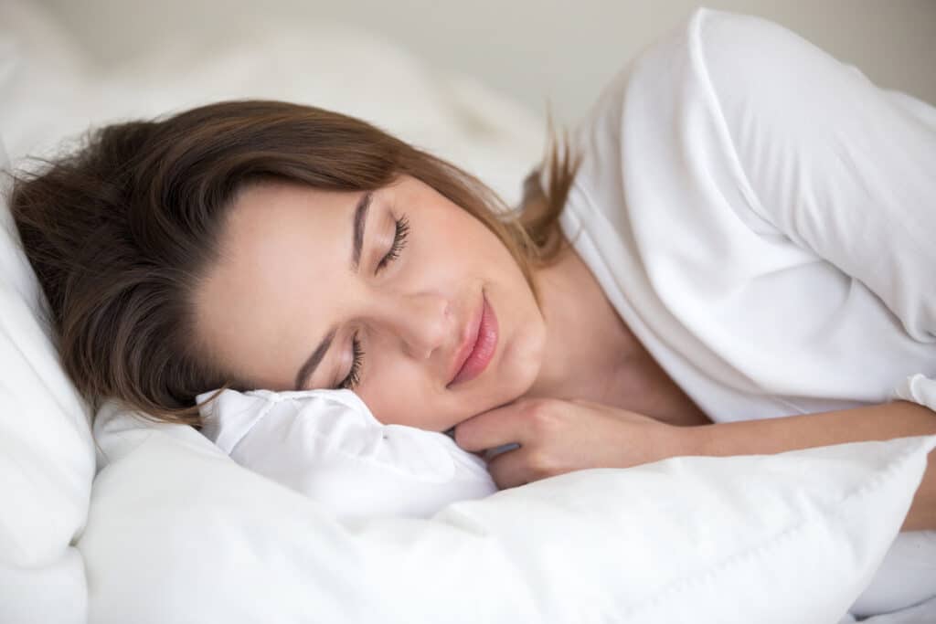 Close-up of a woman peacefully sleeping on a white pillow, symbolizing the goal of achieving restful and restorative sleep through professional sleep consulting.